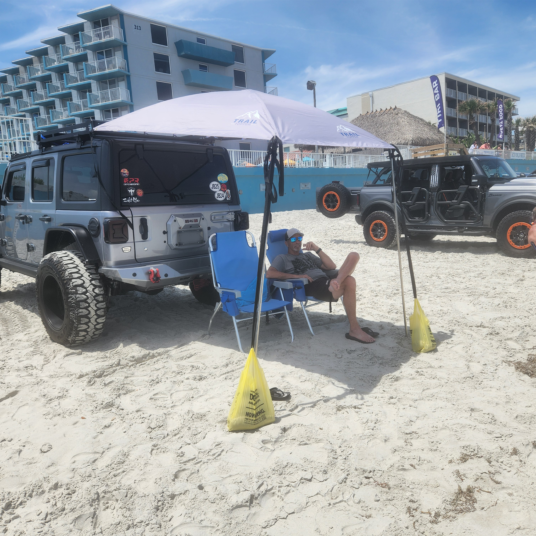 Jeep Wrangler  on a sandy beach in Panama City with a man sitting under a JFTops Adventure Trail Topper shade awning