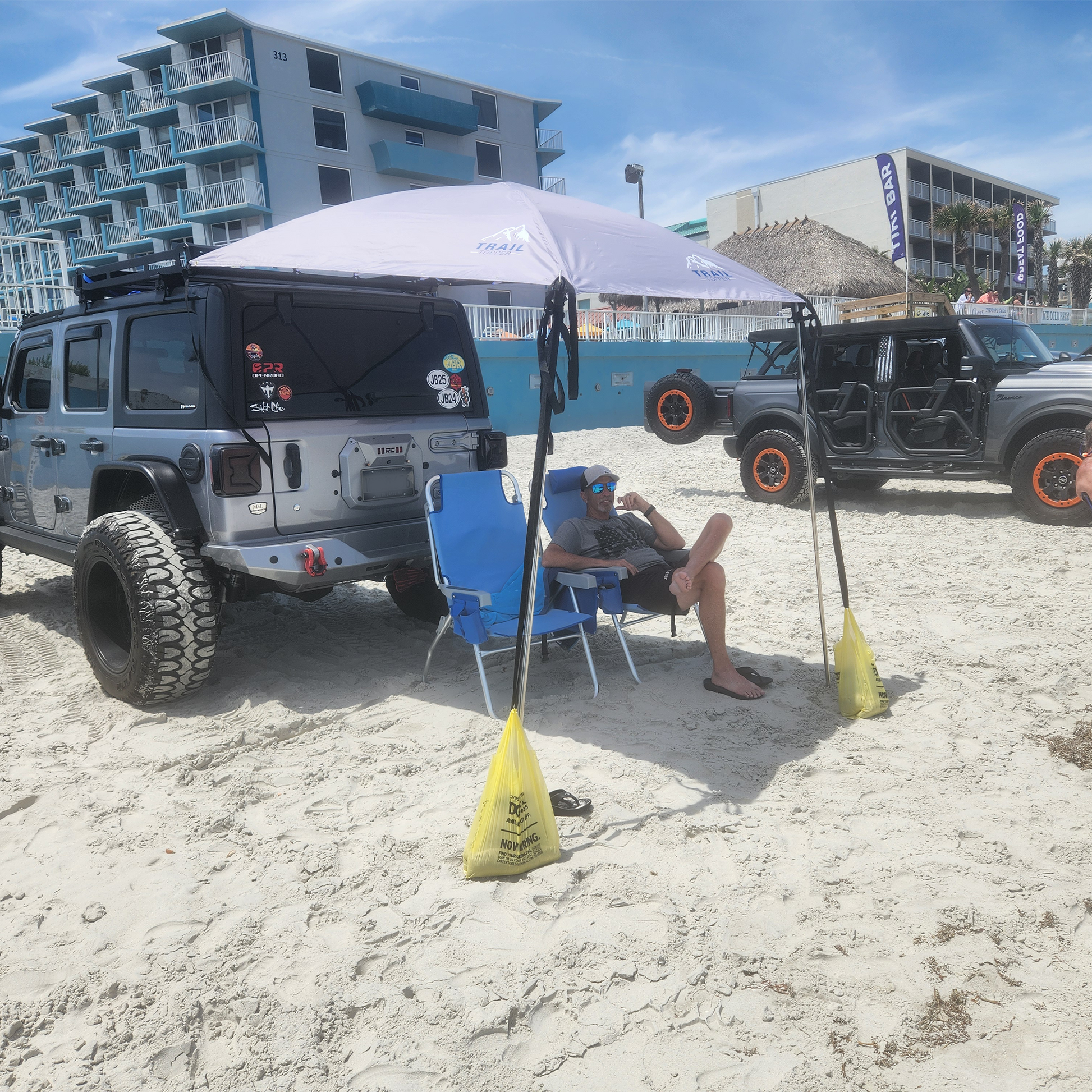 Jeep Wrangler  on a sandy beach in Panama City with a man sitting under a JFTops Adventure Trail Topper shade awning