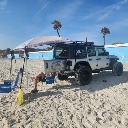 Jeep Wrangler  on a sandy beach with a person sitting under a JFTops Adventure Trail Topper shade awning