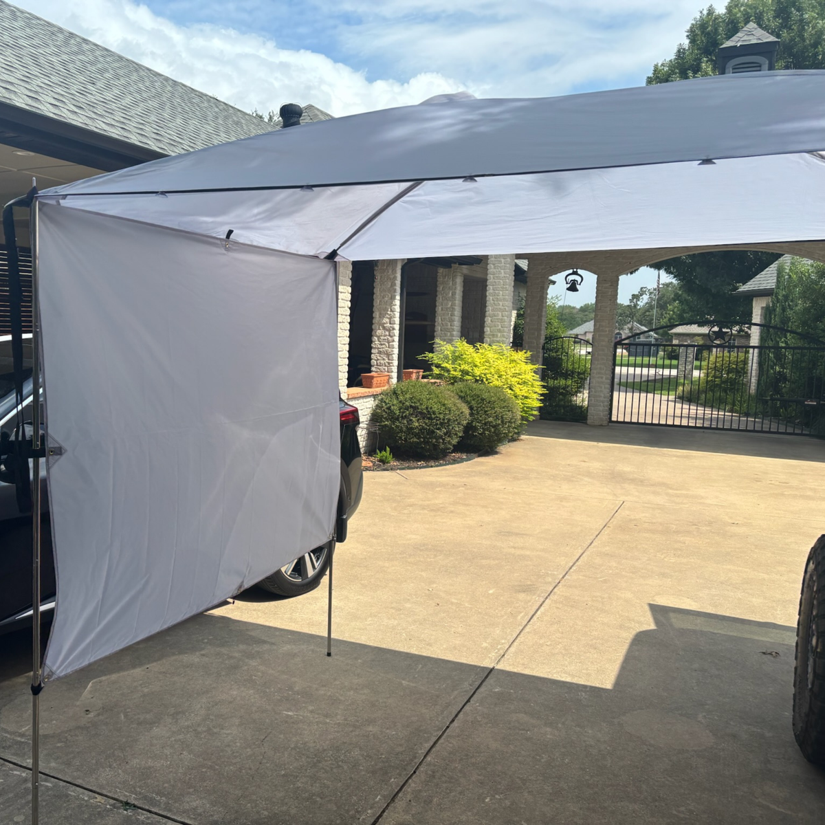 Trail Topper awning with side wall set up on a driveway with a house and driveway in the background.