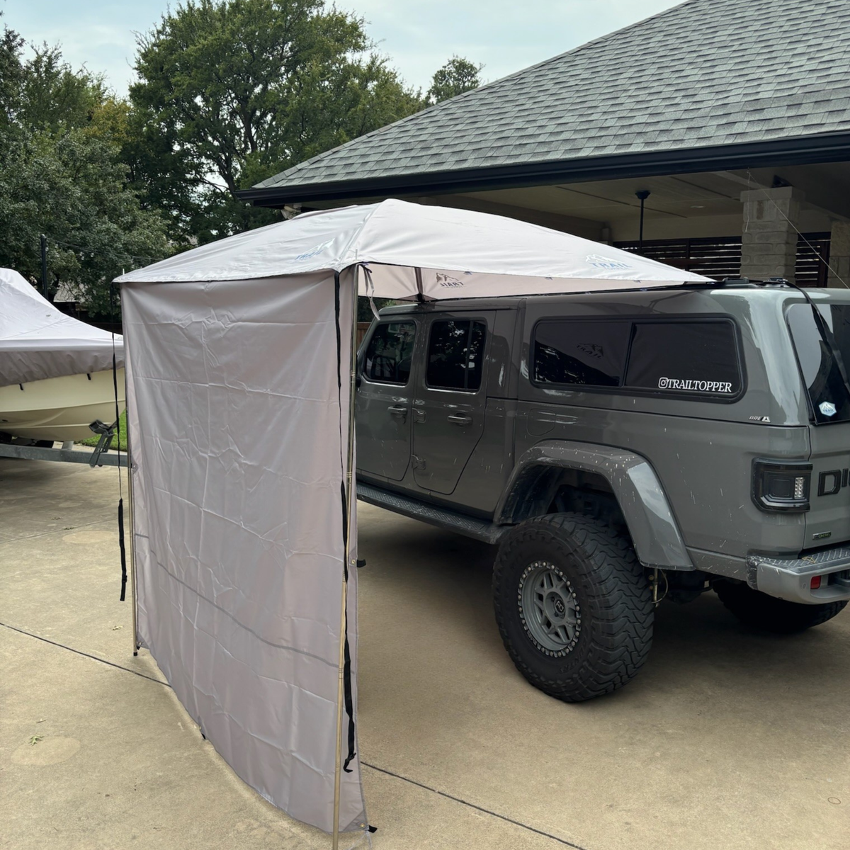 Gladiator parked under a Trail Topper awning with side walls with trees and a building in the background