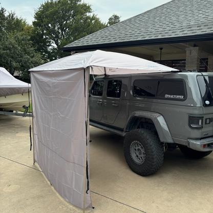 Gladiator parked under a Trail Topper awning with side walls with trees and a building in the background