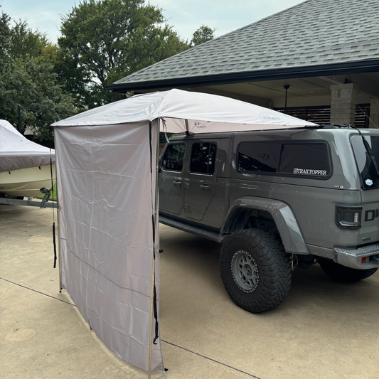 Gladiator parked under a Trail Topper awning with side walls with trees and a building in the background