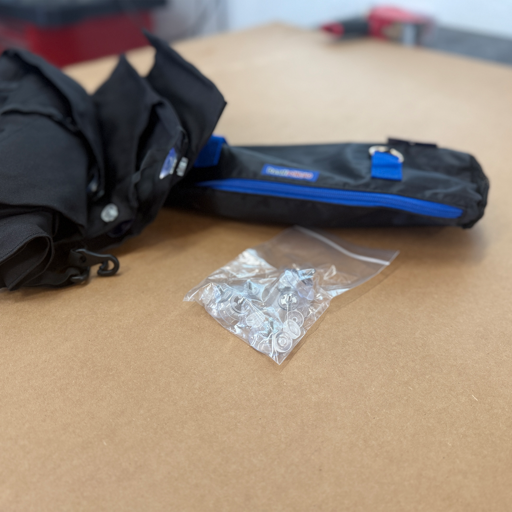Black Dash Poncho, with black bag with blue zipper, and clear plastic bag with 7 replacement suction cups on a brown surface.