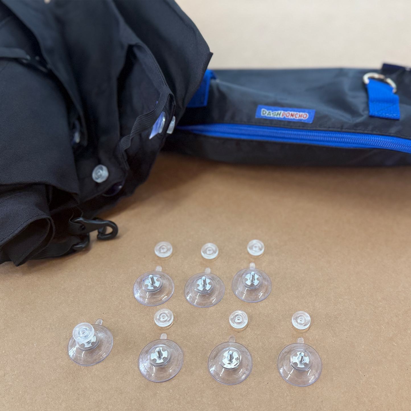 7 Clear suction cups on a brown surface with a black Dash Poncho and  bag in the background.