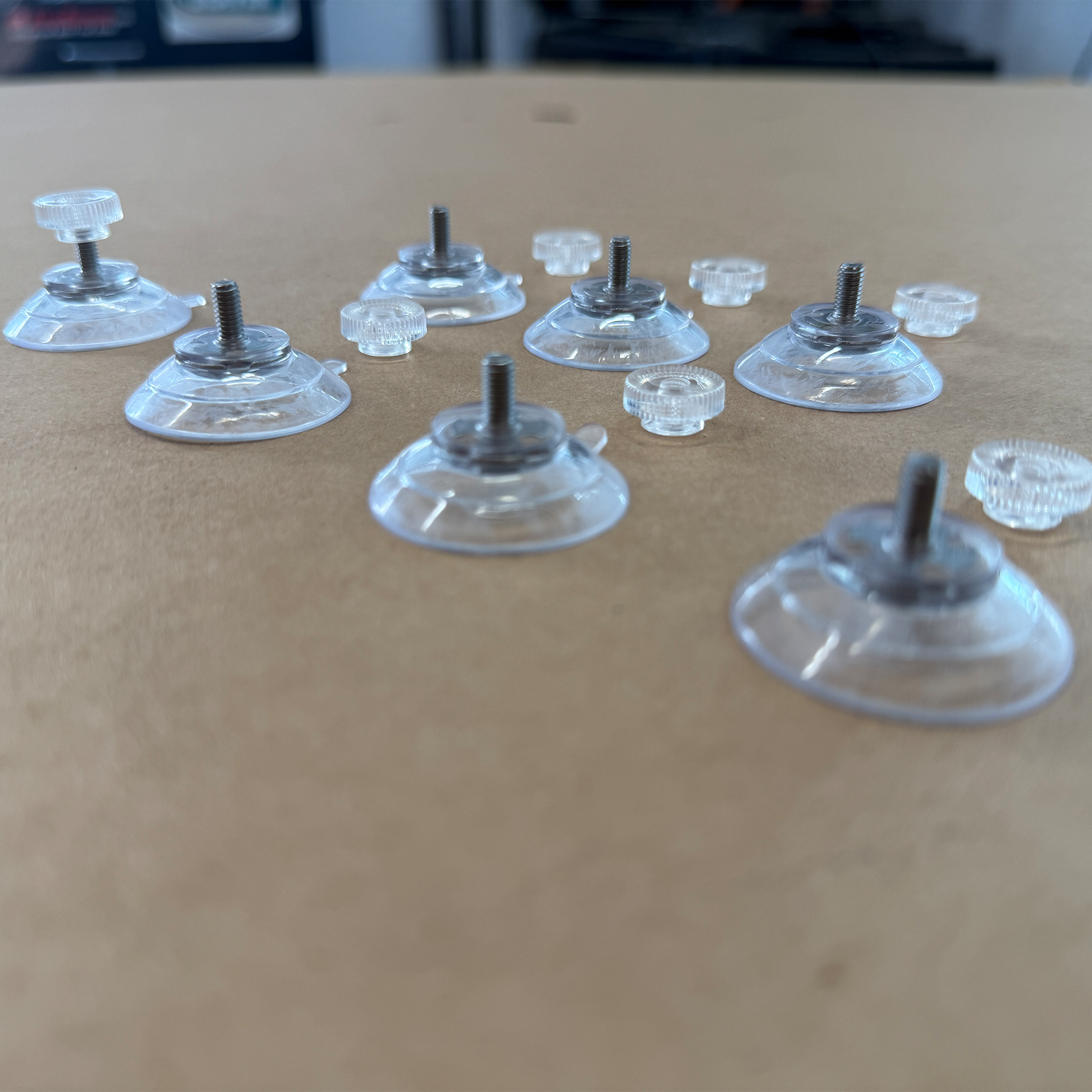 7 Clear suction cups with metal screws on a cardboard surface