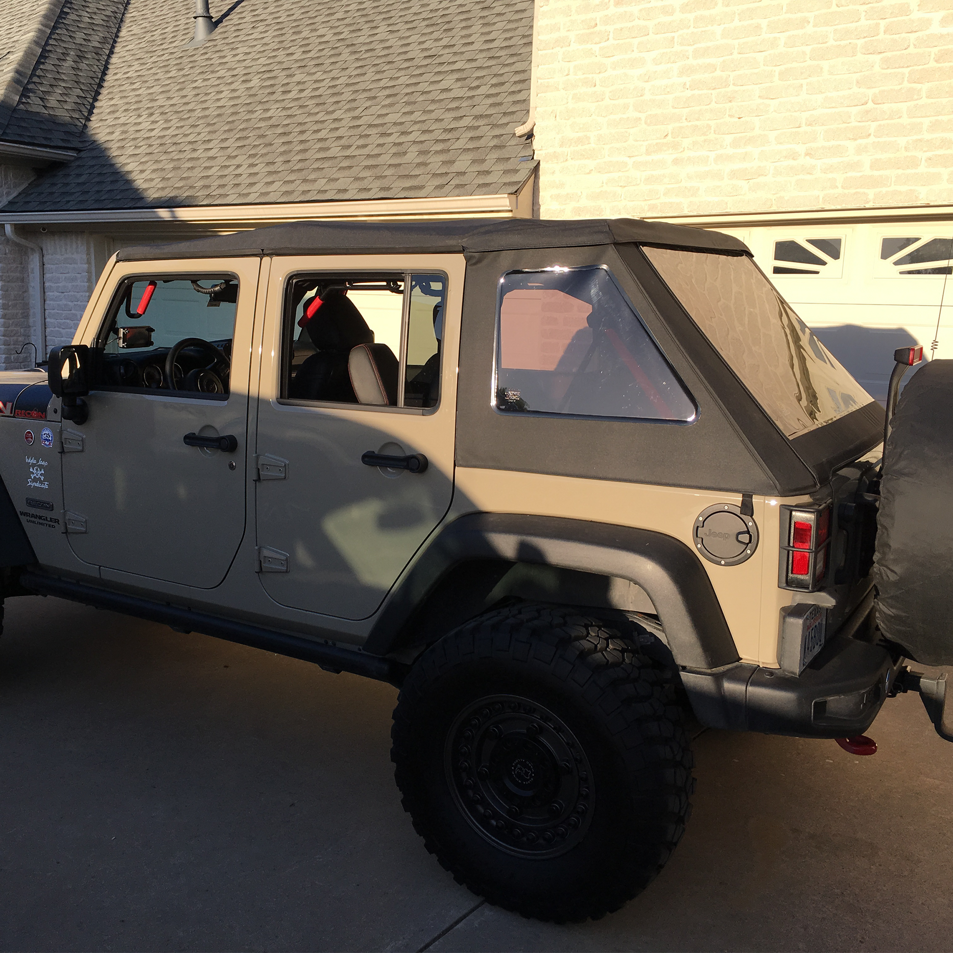 Beige JKU wrangler with black slantback soft top parked in front of a house.