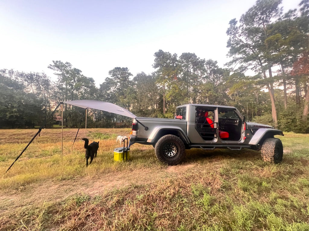 Dogs running in a field with a Jeep Gladiator with Adventure Trail Topper on back