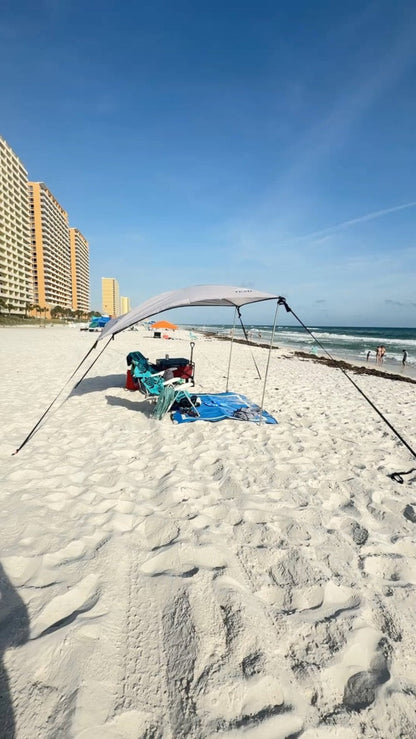 Trail Topper Overland XL on PCB set up on a sandy beach with lounge chairs and towels underneath, with ocean waves and tall beachfront buildings in the background.