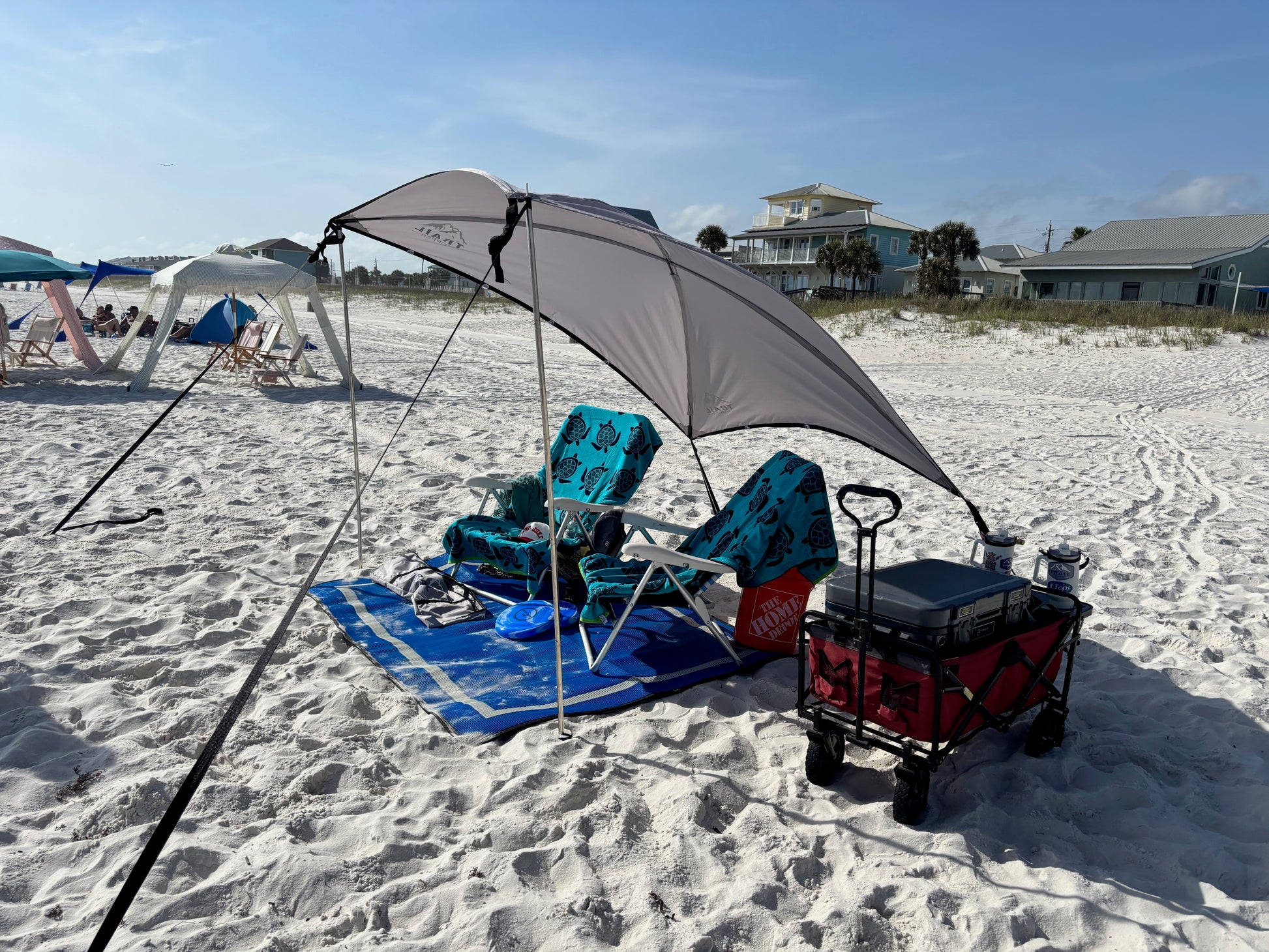 Beach setup with chairs, X-large shade awning, cooler, and cart on sandy beach.