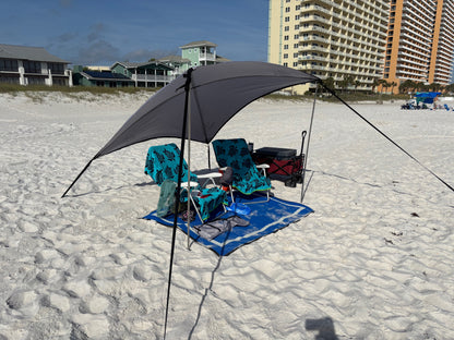 Beach setup with XL Trail Topper awning, chairs, umbrella, and cooler on sandy beach with buildings in the background