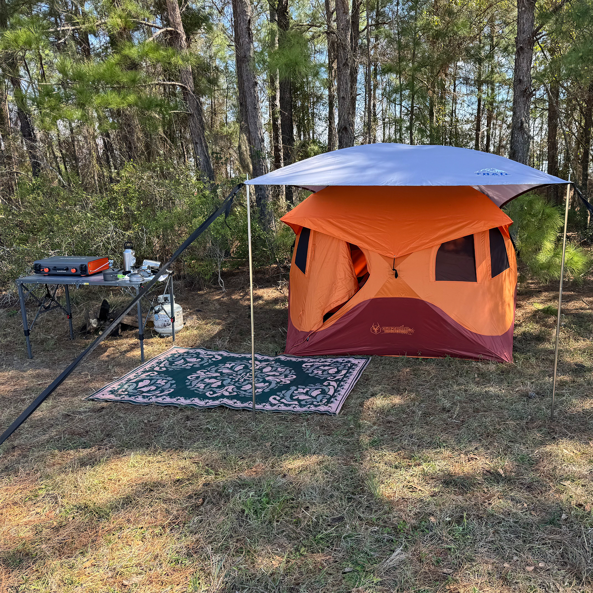 Camping setup with an orange tent and Trail Topper awning over tent for extra shade and heat protection in a forested area.
