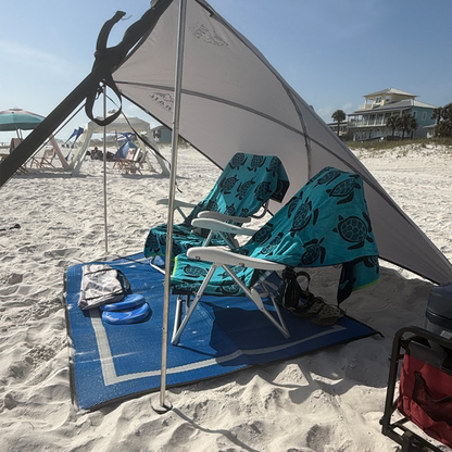 Beach setup with two chairs, towels, and a Trail Topper shade awning on a sandy beach.